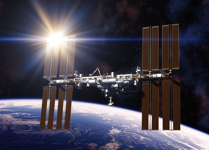 shining light of the sun reflects off of the international space station with the earth in the background